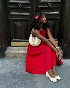 Emmanuelle Koffi usando vestido midi vermelho romântico, bracelete dourado, sapato Tabi branco e shoulder bag branca