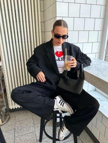 Lara usando blazer preto oversized, baby-tee divertida, bolsa preta básica, calça de alfaiataria e Adidas Samba