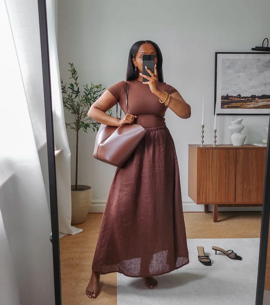 Lydia Tsegay usando camiseta marrom, maxi bag marrom, saia midi de fibra natural marrom e acessórios dourados