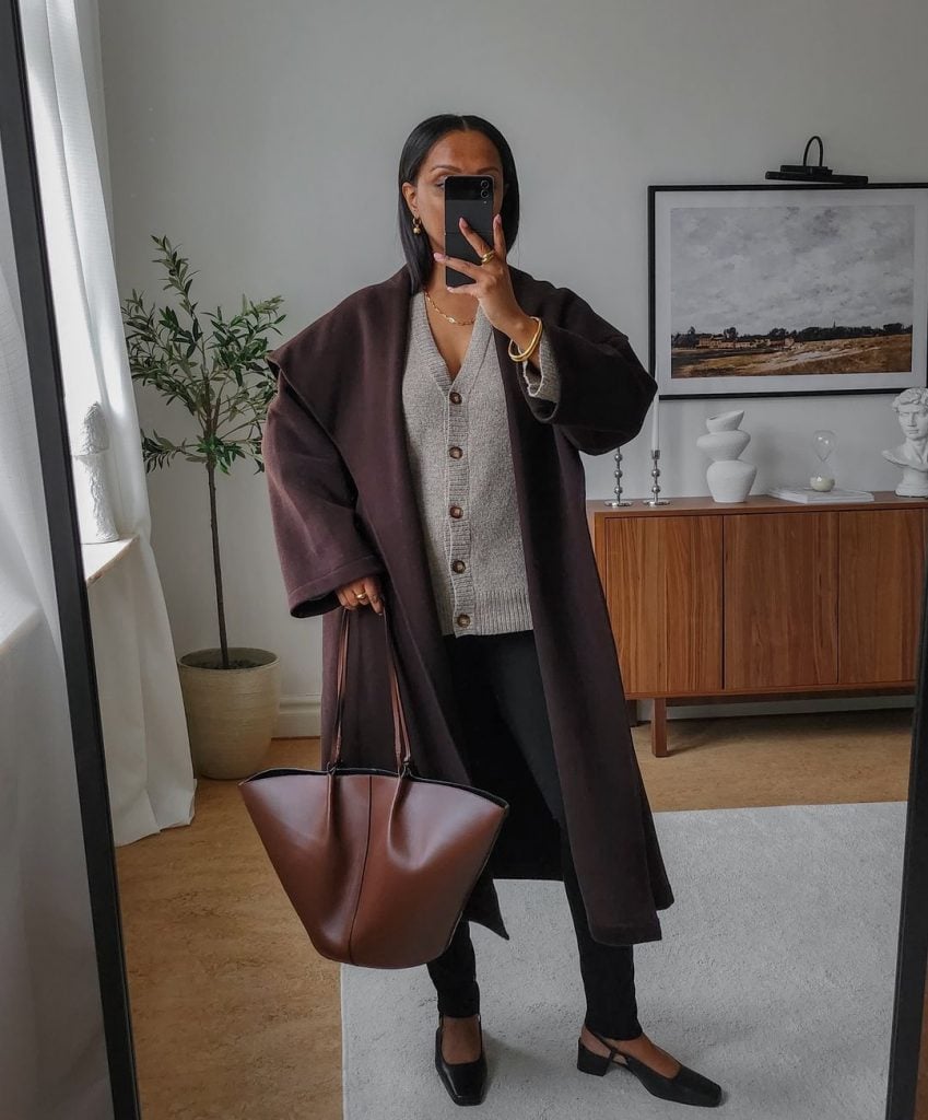Lydia Tsegay usando cardigan cinza, sobretudo marrom, legging preta, bolsa marrom e sapato boneca preto envernizado