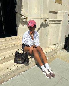 Marilyn usando boné rosa, camisa branca, short de alfaiataria, meia branca aparente e tênis Nike Cortez marrom