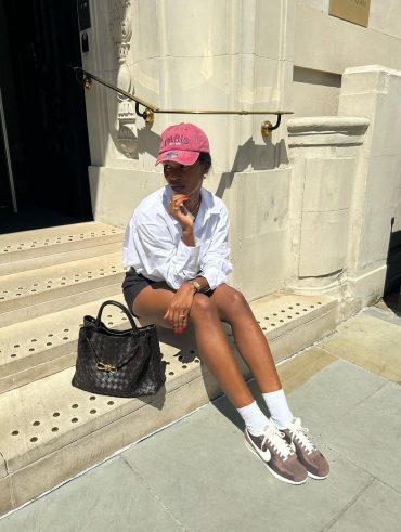 Marilyn usando boné rosa, camisa branca, short de alfaiataria, meia branca aparente e tênis Nike Cortez marrom