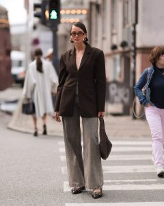 Mary usando óculos de sol de lente transparente colorida, blazer oversized marrom, calça jeans pantalona e slingback Ganni