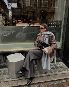Mary usando óculos de sol, cachecol cinza, jaqueta de couro, calça de alfaiataria cinza risca de giz, meia preta e slingback preto kitten heels