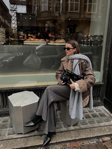Mary usando óculos de sol, cachecol cinza, jaqueta de couro, calça de alfaiataria cinza risca de giz, meia preta e slingback preto kitten heels