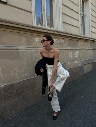 Mary usando óculos minimalista, blusa preta sem alça, calça risca de giz off-white e sapatilha de bailarina