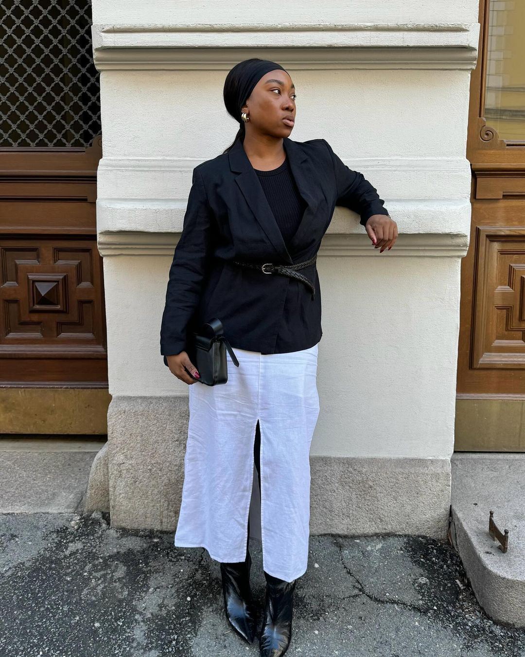 Nnenna usando blazer preto, faixa de cabelo, saia midi branca e bota de cano médio