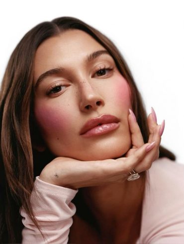 Hailey Bieber com a cabeça apoiada na mão e com blush rosa