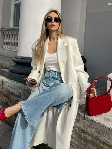 Mulher jovem loira usando sobretudo off-white, calça jeans e slingback vermelho intenso