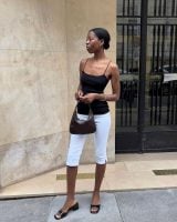 Sylvie Mus usando blusa preta de alça, calça capri branca, shoulder bag minimalista marrom e tamanco