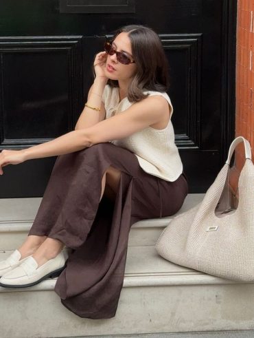 Tia Dewitt usando colete de tricô, saia midi marrom de cetim e loafer off-white