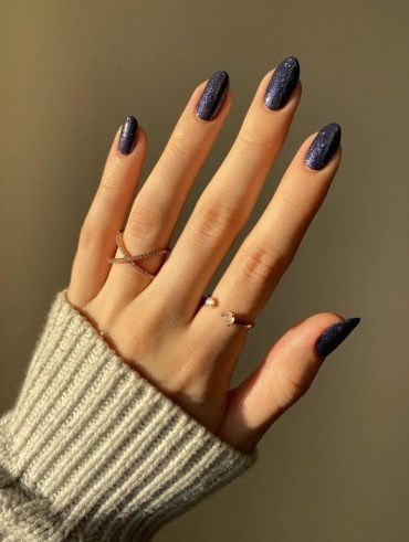 Mão branca com anéis e unha amendoada azul escuro com brilho