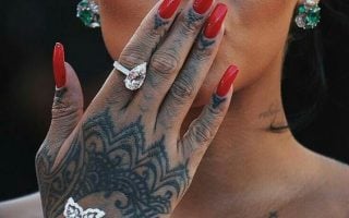 Rihanna com a mão na frente da boca, com anéis e unha bailarina vermelha