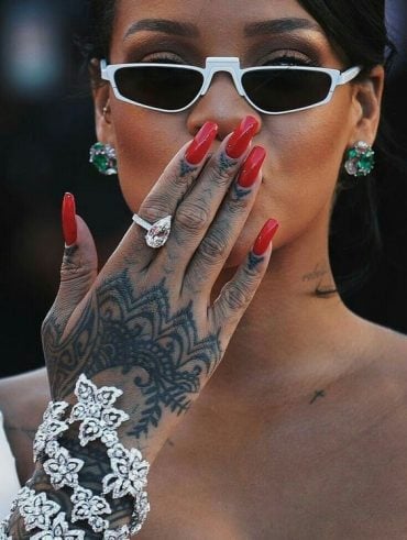 Rihanna com a mão na frente da boca, com anéis e unha bailarina vermelha