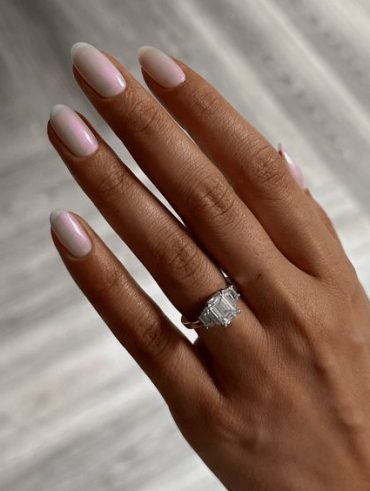 Mão branca com anel e unha arredondada branca cromada com brilho rosa
