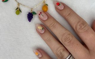 Mão branca com anel prata apoiada no peito com unha amendoada decorada com fruta