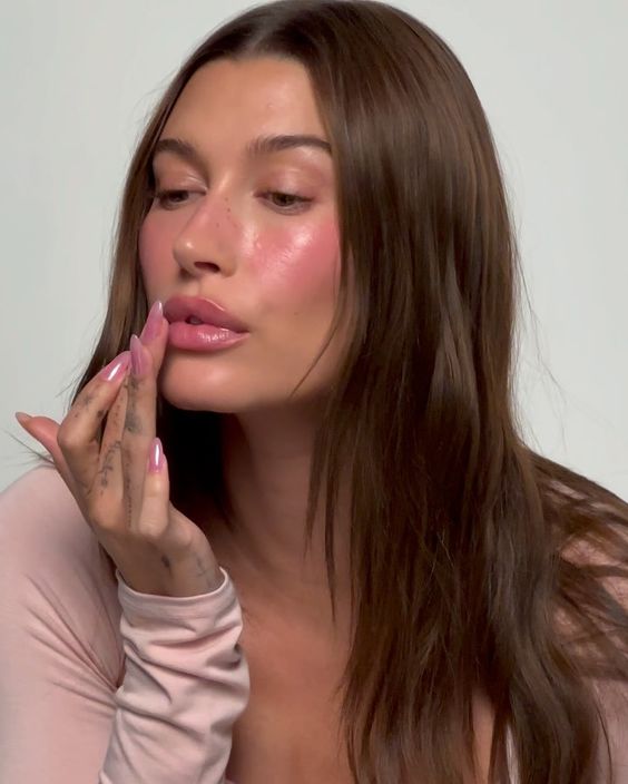 Hailey Bieber com a mãos nos lábios e unha amendoada jelly pink