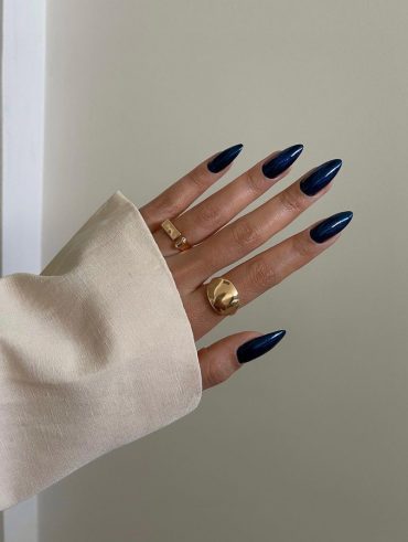 Mão branca com anéis dourados e unha stiletto arredondada azul-marinho