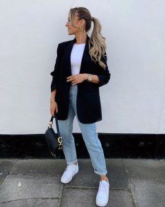 Mulher jovem de pele clara com look com blazer e calça jeans.