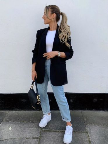 Mulher jovem de pele clara com look com blazer e calça jeans.