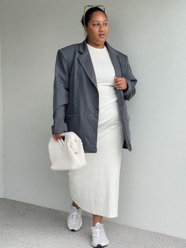 Mulher gorda e negra, usando blazer cinza, vestido de cetim branco e tênis.