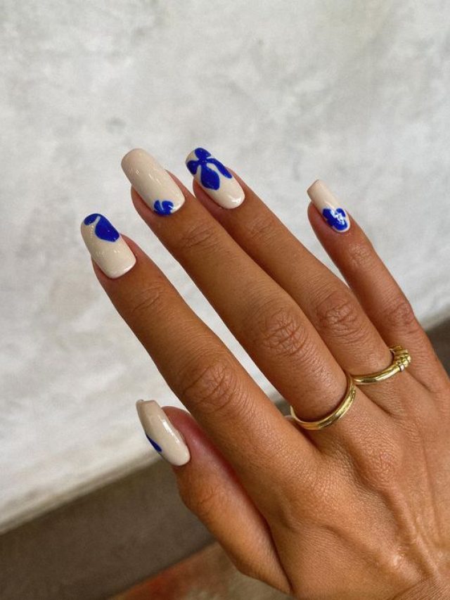 Mão branca com anéis e unha quadrada off-white com decorações em azul