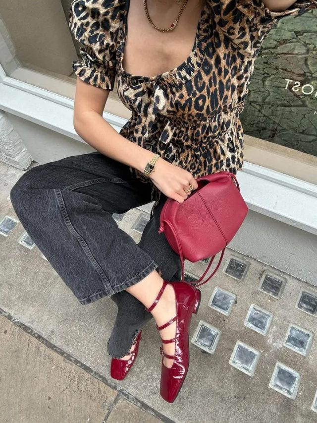 Tia Dewitt usando blusa de oncinha, calça jeans preta, bolsa vermelho cereja e sapatilha Mary Jane vermelho cereja envernizada