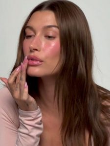 Hailey Bieber com a mãos nos lábios e unha amendoada jelly pink