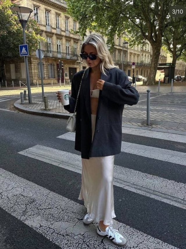 Mulher loira usando blazer preto, vestido de cetim perolado e Adidas Samba.