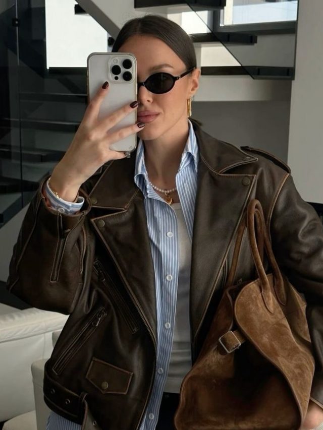 Mulher jovem de pele clara usando jaqueta de couro marrom e camisa azul
