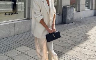Mulher com coque, usando óculos de sol, blazer branco e vestido de cetim.
