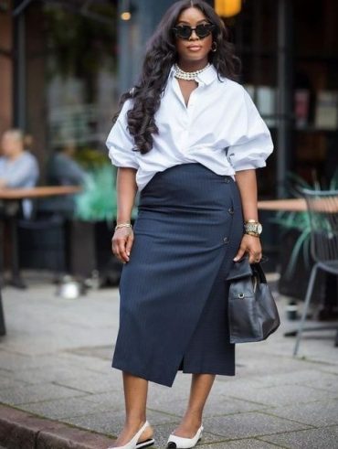 Mulher jovem midsize e pele escura. Ela usa camisa branca e saia midi preto com calçado slingback.
