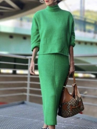 Mulher madura, com cabelo curto e grisalho, usando óculos, blusa e saia em cor verde e usando tênis Vans.