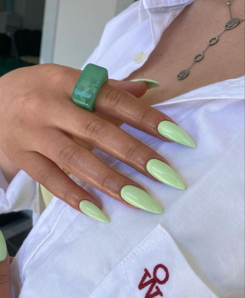 Mão com anel grande em cor verde, unhas compridas e pintadas de verde-claro