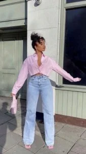 Mulher jovem e negra, usando camisa cropped rosa e calça jeans.