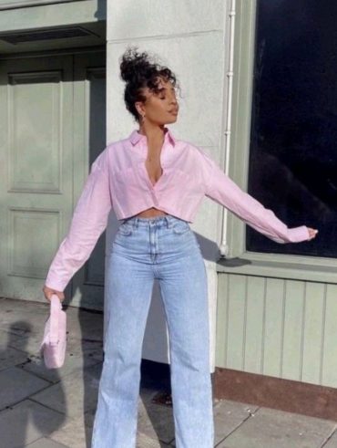 Mulher jovem e negra, usando camisa cropped rosa e calça jeans.