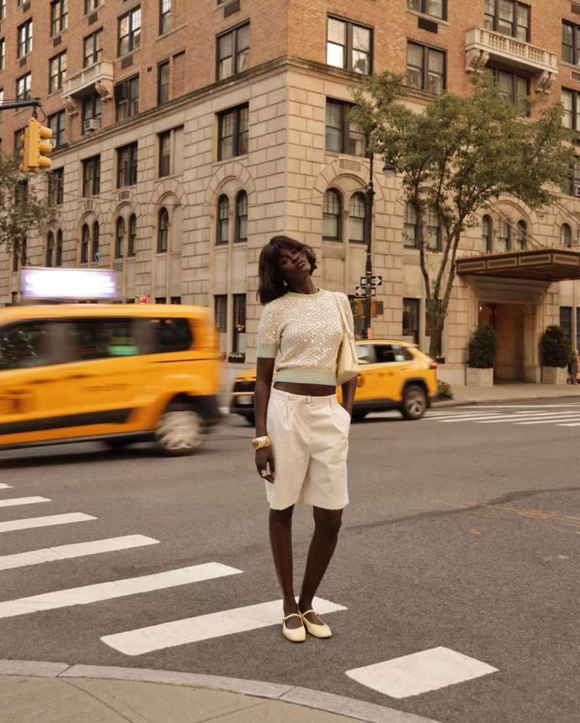 Amy Julliette Lefévre usando blusa de paetê, bolsa amarelo-manteiga, bracelete dourado, bermuda de alfaiataria branca e sapatilha amarelo-manteiga