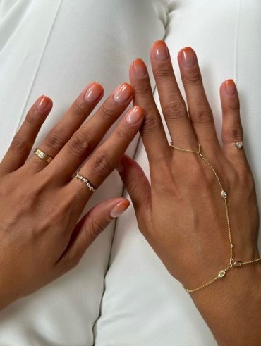 Mão branca com anéis dourados e unha curta quadrada ombré laranja