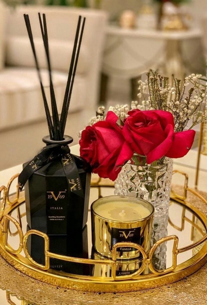 Bandeja dourada com rosas vermelhas, vela e aromatizador de ambientes