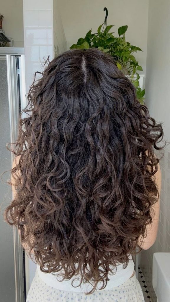 Mulher com cabelo longo e ondulado, de curvatura 2C, com corte em U