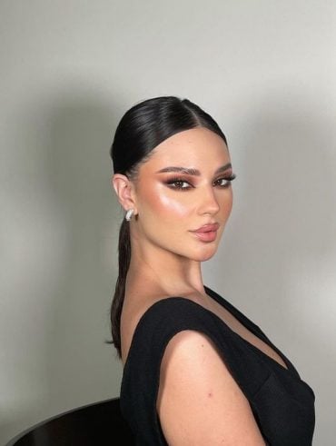 Mulher branca com cabelo preto, vestido preto e make neutra com cílios grandes