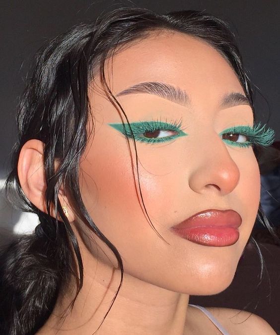 Mulher branca com cabelo escuro e sombra verde com máscara de cílios verde