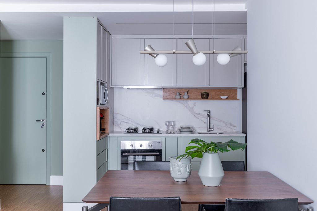 Cozinha com armários cinza e verde menta, com mesa pequena