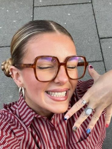 Mulher branca com camisa listrada, coque e maquiagem com óculos
