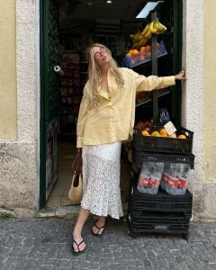 Julia usando camisa amarelo-manteiga, saia midi de renda, bolsa de palha e chinelo de dedo