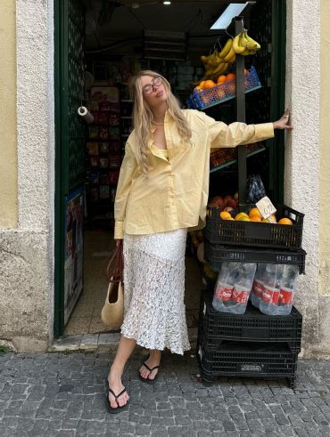 Julia usando camisa amarelo-manteiga, saia midi de renda, bolsa de palha e chinelo de dedo