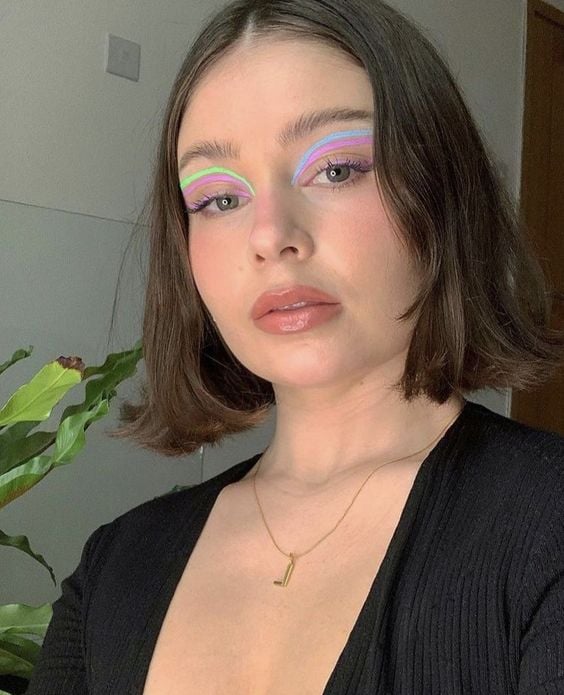 Mulher branca com roupa preta, cabelo escuro curto e maquiagem com delineado gráficos cores pastel
