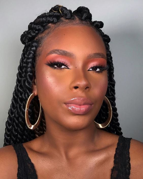 Mulher de pele negra, com regata preta, cabelo escuro trançado e maquiagem colorida 