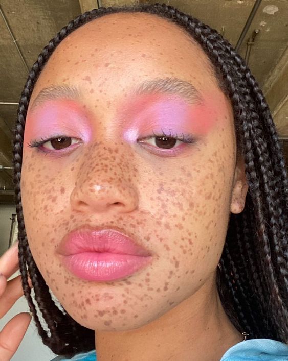 Mulher negra com sardas, cabelo trançado e maquiagem com sombra rosa pastel