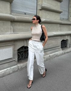 Mary usando óculos de sol, blusa de tricô gola alta off-white, calça de alfaiataria branca e chinelo kitten heels